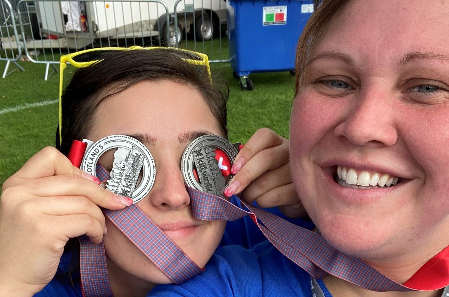 Two women smiling at camera. One is holding silver medals over her eyes